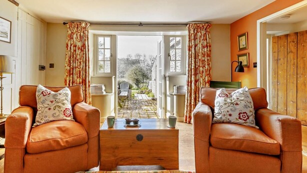A living room with two leather armchairs, a wooden coffee table, and a view through a glass door to a garden. - 3 Bed in Wells-next-the-sea (oc-ncc68) (Stiffkey)