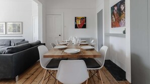 Un'area pranzo moderna con un tavolo in legno apparecchiato per quattro persone, sedie bianche, una lampada a sospensione grigia e una porta che dà su un'altra stanza.