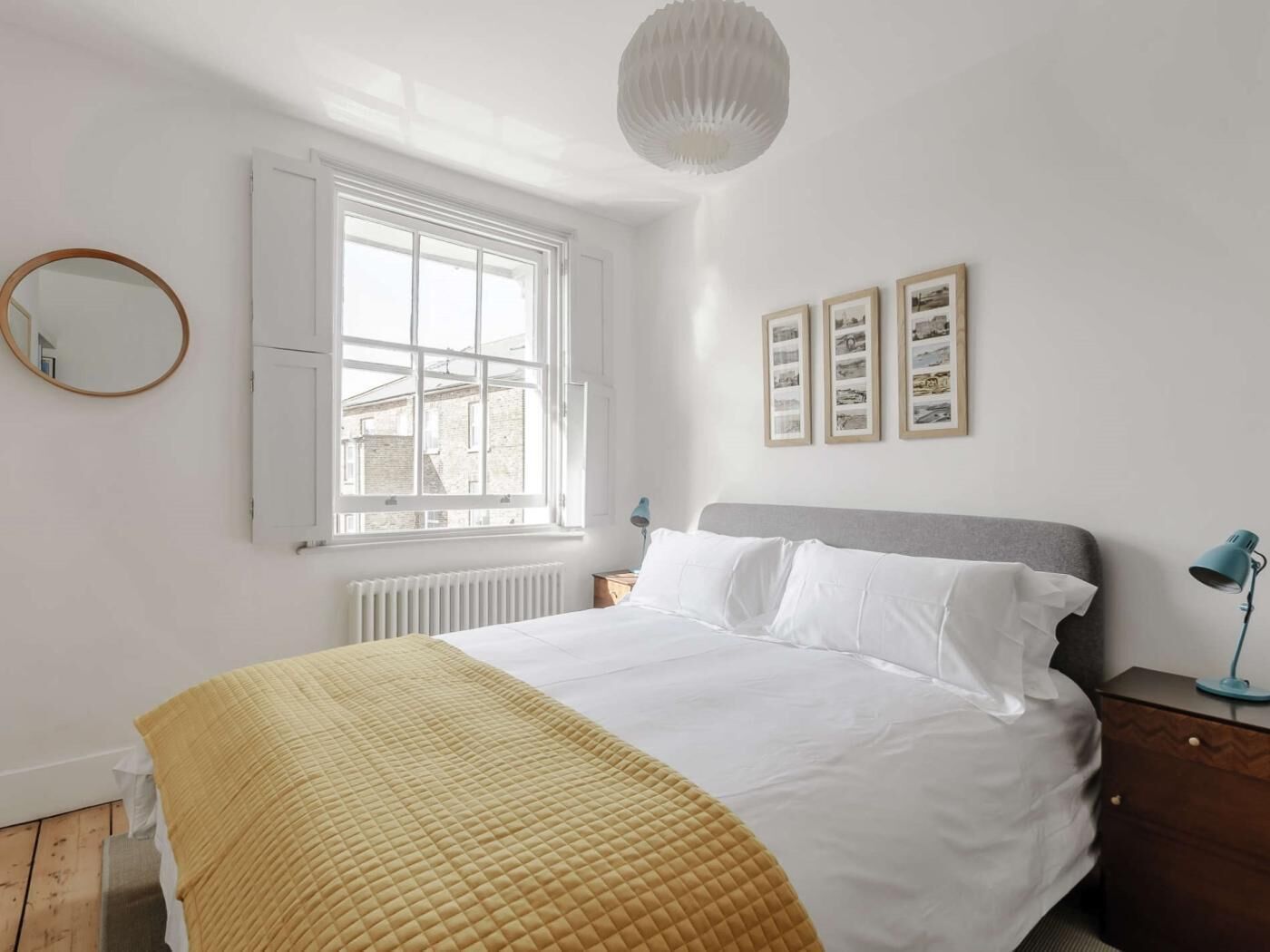 Een slaapkamer met een bed, een raam, een radiator, een nachtkastje, een lamp en wanddecoratie.