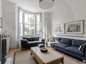 Ein modernes Wohnzimmer mit großem Fenster, zwei Sofas, einem Couchtisch und gerahmten Kunstwerken an den Wänden.