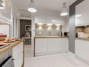 A modern kitchen with white cabinets, a wooden countertop, and pendant lighting.