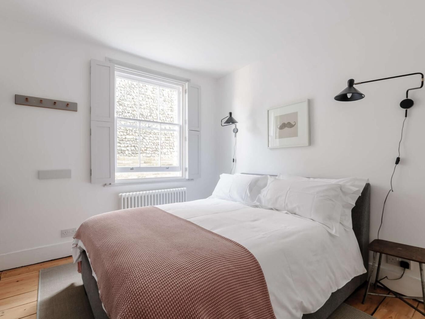 Un dormitorio con cama, ventana, radiador, estante en la pared y un marco de foto.
