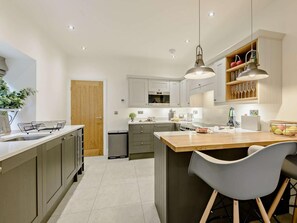 Eine moderne Küche mit grauen Schränken, einer Holztür, einem Edelstahlspülbecken und einer Theke mit Hockern.