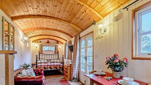 Una habitación acogedora con techo de madera, una cama, una mesa roja con sillas y una ventana con cortinas.