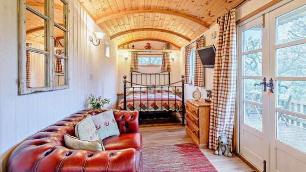 Un dormitorio acogedor con techo de madera, una cama, un sofá de cuero y un ventanal grande.