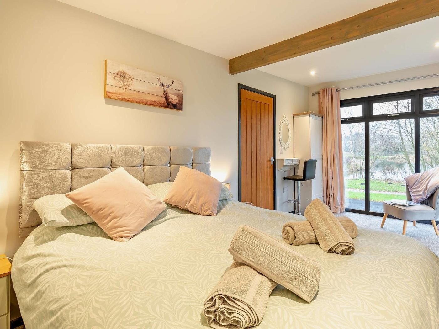 A bedroom with a large bed, a headboard, a painting, a wardrobe, a chair, and a view of the outdoors.