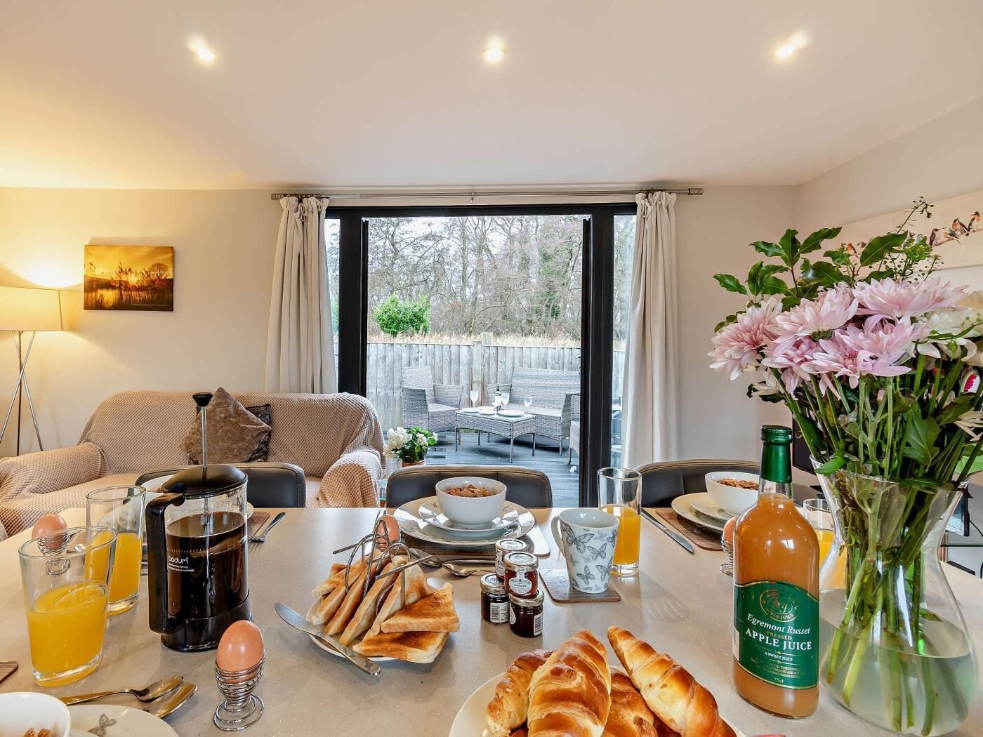 Une table de petit-déjeuner avec des toasts, des œufs, du jus d’orange et une bouteille de jus de pomme.