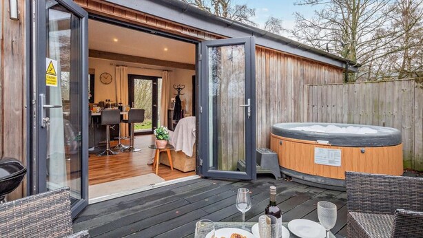 Terraza de madera con jacuzzi, mesa de comedor y mobiliario de exterior.
