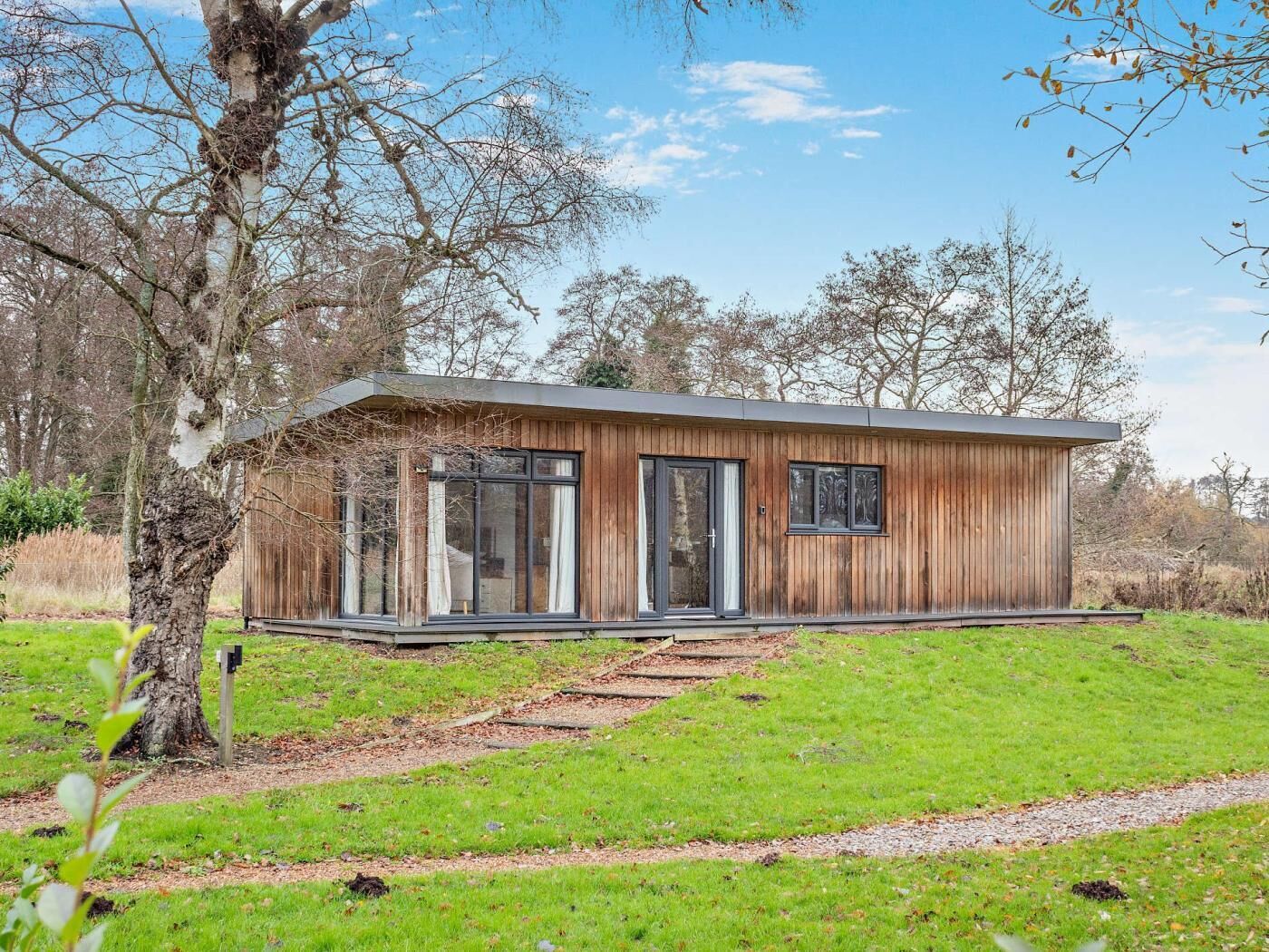 Une cabane moderne en bois, de plain-pied, dotée de grandes fenêtres et d’un porche abrité.