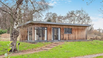 Une cabane moderne en bois, de plain-pied, dotée de grandes fenêtres et d’un porche abrité.