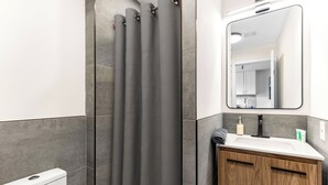 Un bagno moderno con tenda doccia, uno specchio, un lavandino e un water.