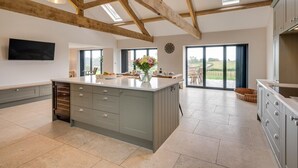 A spacious kitchen with a large island, wooden beams, and a view through the glass doors. - 4 Bed in Bedale (oc-80704) (Newton-le-Willows)