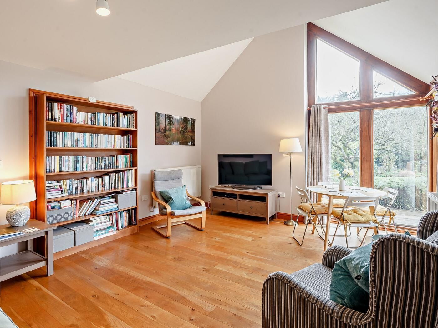 A cozy living room with a bookshelf, a TV, a dining area, and a large window.