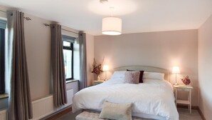 Ein Schlafzimmer mit einem großen Bett, Nachttischlampen, einem fenster mit Vorhängen, einer Heizung und einer Bank.