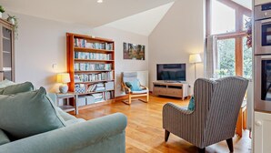 Ein Wohnzimmer mit Bücherregal, Fernseher, Sofa und einem gestreiften Sessel.