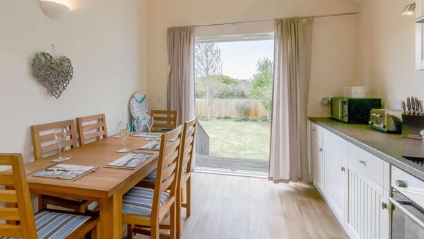 Comedor con una mesa y sillas de madera, un adorno en forma de corazón y vista a un jardín a través de un ventanal.