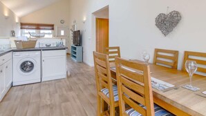 Una cocina compacta con lavadora, un comedor con sillas de madera y una mesa, y una decoración de pared con forma de corazón.