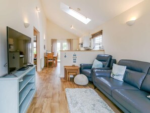 A modern living room with a flat-screen TV, a leather sofa, and a dining area with a wooden table and chairs.