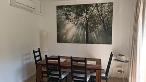 Une salle à manger avec une table en bois, des chaises noires, un lustre et un tableau sur le mur représentant une forêt.