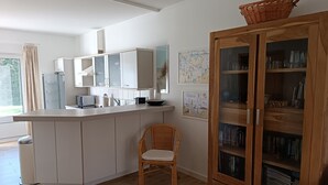 Une cuisine moderne avec des meubles blancs, une chaise en osier et un meuble en bois doté de portes en verre.