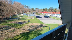 On aperçoit un parking avec plusieurs voitures, une zone herbeuse et une rangée de bâtiments aux toits rouges.