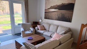 Un salon comprenant un canapé, des fauteuils, une table basse et un tableau représentant un paysage.
