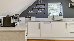 Une cuisine moderne avec des meubles blancs, une machine à café et une fenêtre équipée de stores.