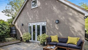 Une maison avec une terrasse en pierre, un banc en bois et un canapé avec des coussins.