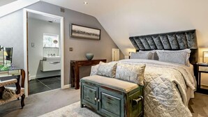 Une chambre avec un plafond en pente, un lit doté d’une tête de lit capitonnée, un banc et une commode.