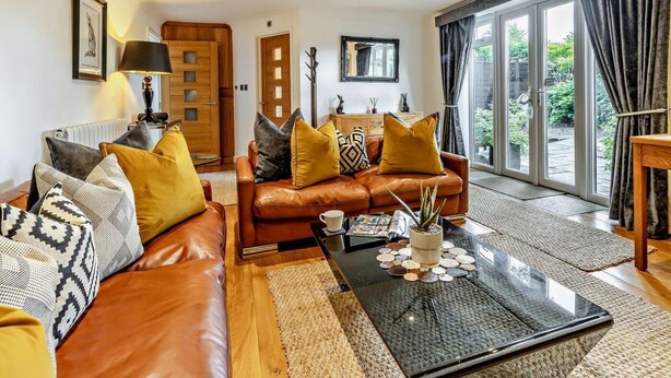 Un salon moderne avec un canapé en cuir, une table basse agrémentée d’objets décoratifs, une cheminée et une grande porte-fenêtre coulissante donnant sur un jardin.