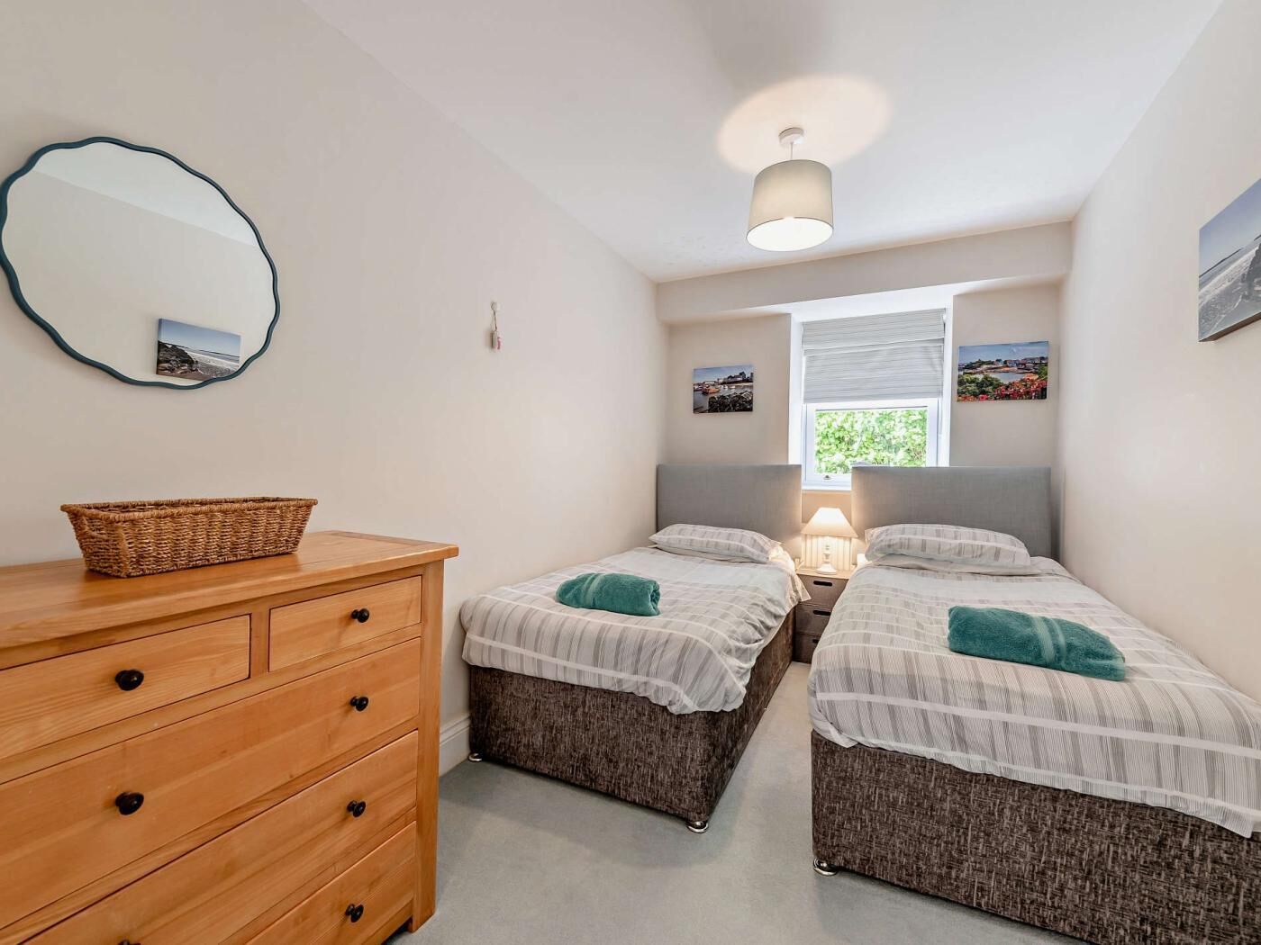 Une chambre avec deux lits simples, une commode en bois, un miroir et une fenêtre donnant sur un paysage agréable.