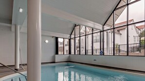 Una piscina interior con paredes de vidrio transparente, suelo de baldosas y una marca de profundidad.