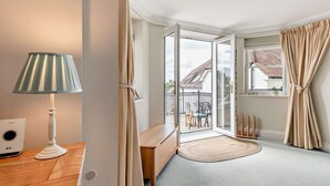 Un dormitorio moderno con un gran ventanal corredera a un balcón, una mesita de noche con lámpara y vistas al exterior.