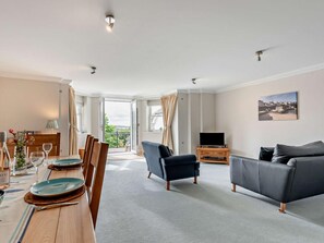 Ein modernes Wohnzimmer mit Essbereich, einem Balkon und Blick sowie einem Flachbildfernseher.