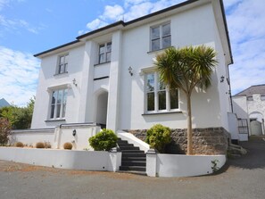 A two-story building with a white exterior, a staircase leading to the entrance, and a palm tree in the front yard. - 3 Bed in Tenby (oc-73606) (Tenby)