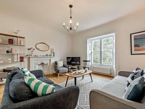A living room with a fireplace, a television, and a large window. - 3 Bed in Tenby (oc-73606) (Tenby)