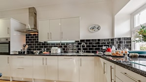 Una cocina moderna con armarios blancos, salpicadero negro y una campana extractora de acero inoxidable.