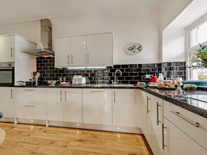 A modern kitchen with white cabinets, black backsplash, and a stainless steel range hood. - 3 Bed in Tenby (oc-73606) (Tenby)