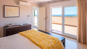 Hotelkamer met een bed, nachtkastje, bureau, airconditioning, een ingelijste foto en uitzicht op zee door een schuifdeur.