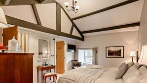 Ein Schlafzimmer mit Bett, Schreibtisch, Stuhl, Kommode, Spiegel, einer Chandelüster und einem Fenster.