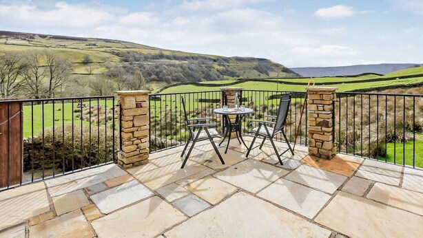 Eine Terrasse mit Steinbelag, zwei Stühle, ein Tisch und eine Steinsäule.