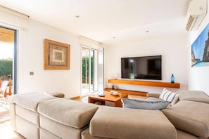 Ein modernes Wohnzimmer mit einem großen Flachbildfernseher, einem Holztisch und einem beigefarbenen Sofa.