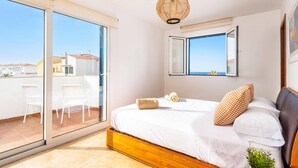 A bedroom with a large bed, a window with a view, a ceiling fan, and a balcony with chairs. - Villa Nile by Villa Plus (Los Delfines)