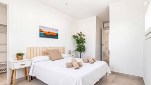 A bedroom with a bed, a nightstand, a wall-mounted painting, a potted plant, and a door leading to another room. - Villa Nile by Villa Plus (Los Delfines)