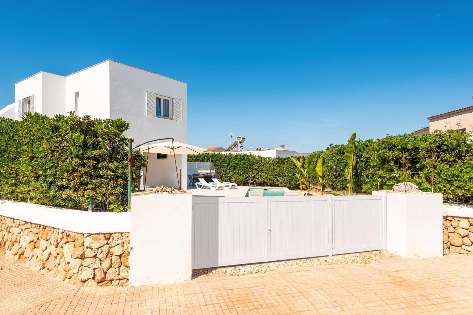Una villa moderna con piscina, paredes blancas y un muro de piedra.
