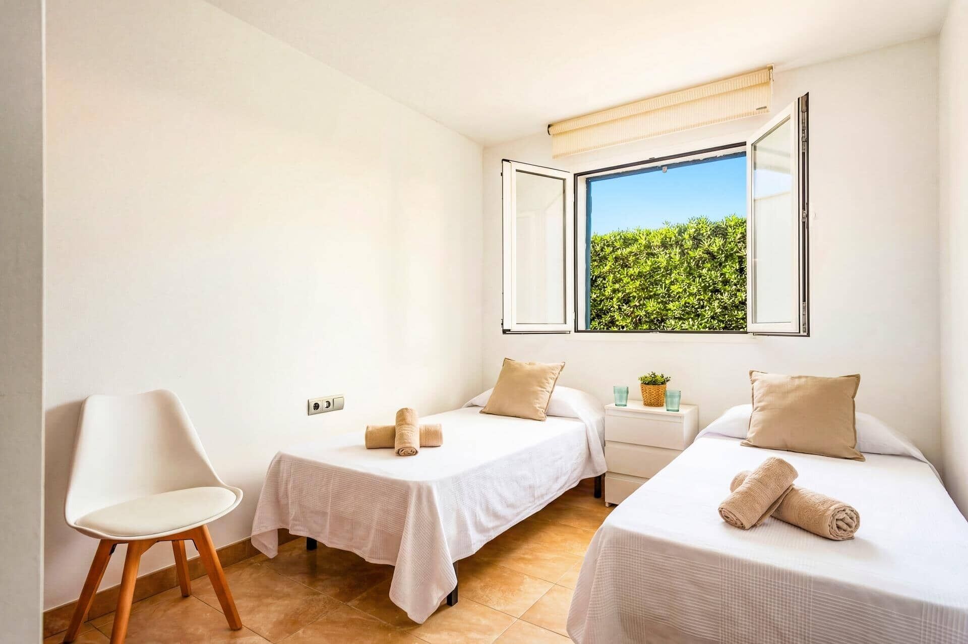 Ein Hotelzimmer mit zwei Betten, einem Sessel, einem kleinen Tisch und einem Fenster mit Blick ins Grüne.