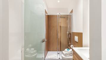 Ein modernes Badezimmer mit einer Duschkabine aus Glas, einer Wandverkleidung aus Holz, einer weißen Toilette und einem Waschbecken mit Holzablagefläche.