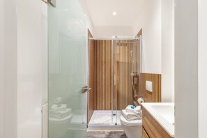 A modern bathroom with a glass shower enclosure, a wooden panel wall, a white toilet, and a sink with a wooden countertop. - Furnished Radebeul Studio Apartment with Balcony and Wi-Fi (Radebeul)