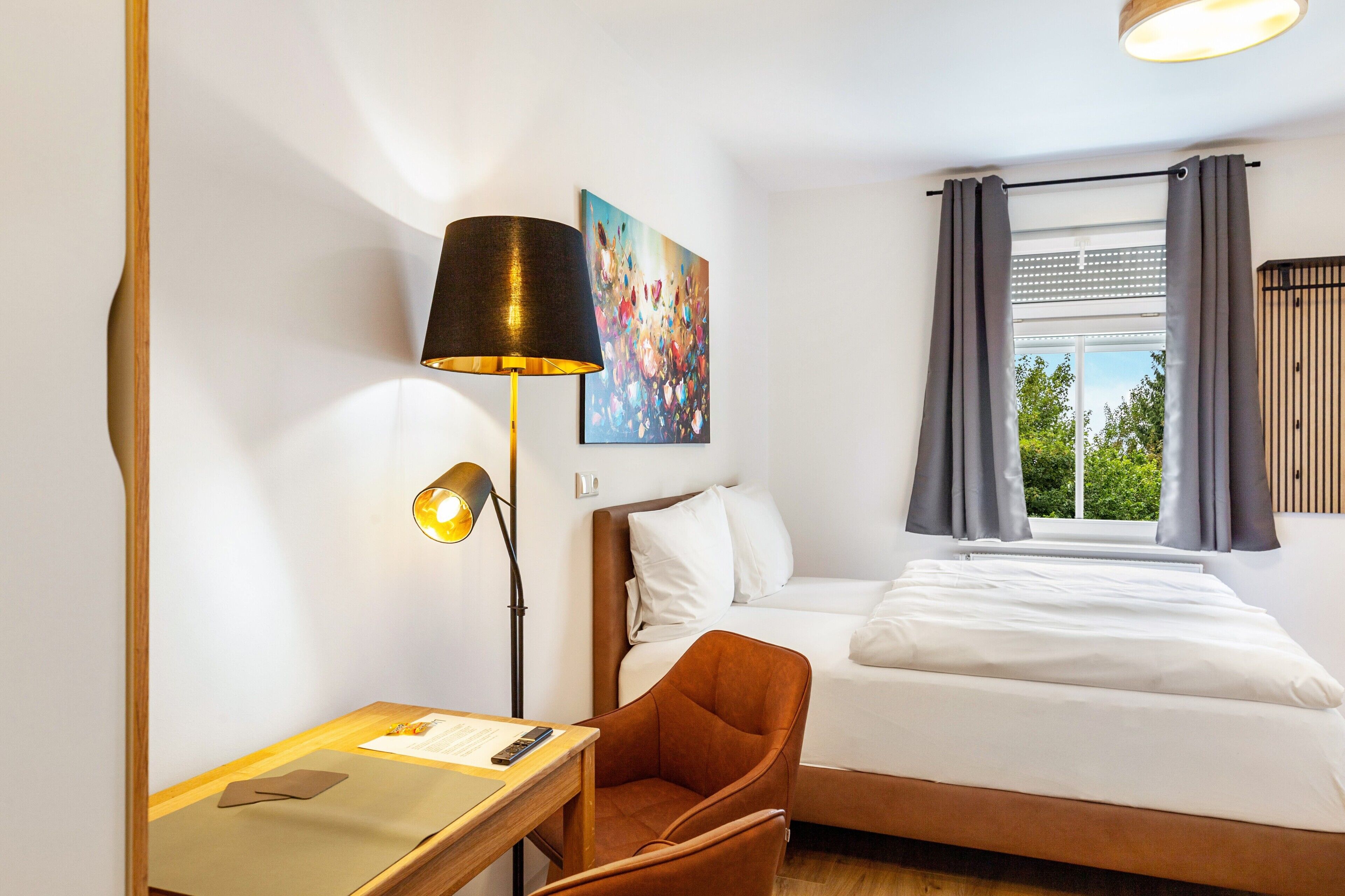 Habitació d'hotel amb un llit, escriptori amb làmpada, cadira i un quadre a la paret.