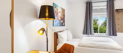 Una habitación de hotel con cama, escritorio con lámpara, silla y un cuadro en la pared.